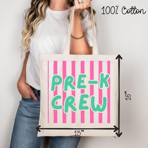 May include: A cream tote bag with pink vertical stripes and the words "PRE-K CREW" in green. The bag is 38 cm wide and 41 cm tall, made of 100% cotton.