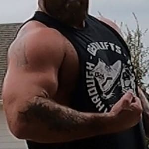 Puede incluir: Un hombre con una camiseta negra sin mangas con un gráfico blanco que dice "Tough-Lifts" y una bandana negra. Está flexionando su bíceps.
