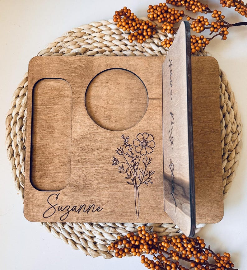 May include: A personalized wooden tray with a cutout for a mug, a phone slot, and a floral design. The tray is engraved with the name "Suzanne" and the text "Starts a New Chapter".