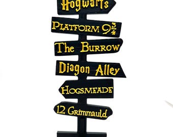 May include: Black wooden signpost with gold lettering pointing to various locations from the Harry Potter universe, including Hogwarts, Platform 9 3/4, The Burrow, Diagon Alley, Hogsmeade, and 12 Grimmauld Place.