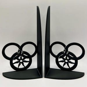 May include: A pair of black bookends featuring a stylized design of three interlocking circles with a starburst in the center.