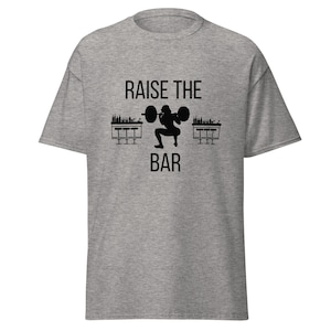 May include: A gray t-shirt with the text "RAISE THE BAR" and a silhouette of a person lifting a barbell above two bar stools.