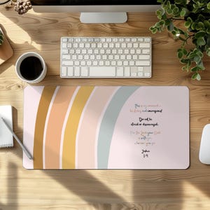 May include: A rectangular mouse pad with a pastel rainbow design in shades of peach, gold, and blue. The pad features inspirational text from Joshua 1:9. A keyboard, coffee cup, and other office supplies are visible.