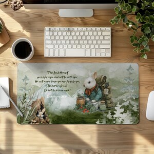 May include: A rectangular mousepad featuring a watercolor illustration of a white rabbit with a backpack, scarf, and jacket, set against a mountain backdrop. Text from Deuteronomy 31:8 is included. The mousepad is on a wooden desk with a keyboard and coffee cup.
