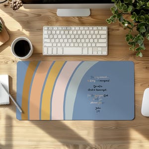 May include: A rectangular desk mat featuring a blue background with a series of curved, vertical stripes in shades of mustard yellow, peach, and light gray. The text reads: This is my command... be strong and courageous! Do not be afraid or discouraged. For the Lord your God is with you, wherever you go. Joshua 1:9.