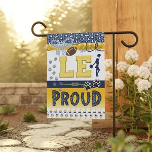 May include: A garden flag with a blue and gold design. The flag features the text "LE PROUD" with paw prints, a football, and a cheerleader silhouette. The top border has a leopard print pattern.