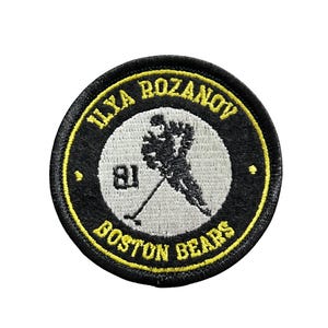 May include: Round black and yellow patch featuring the text "ILYA ROZANOV" and "BOSTON BEARS". The patch has a central image of a hockey player in black and white, with the number "81".