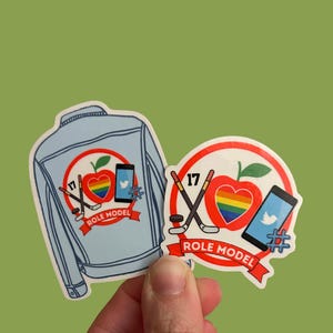 May include: Two stickers with a light blue denim jacket and a round design. The designs include a rainbow heart apple, hockey sticks, a smartphone with a Twitter logo, and the text "ROLE MODEL" on a red banner. The number "17" is also included.