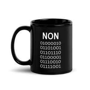 May include: A black ceramic mug with the word "NON" in white, followed by a series of binary code numbers. The mug has a curved handle and a glossy finish. The design is simple and modern.