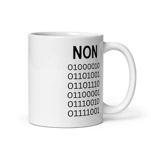 May include: White ceramic mug with the word "NON" in bold black letters, followed by a series of binary code numbers. The mug has a curved handle and a glossy finish, suitable for hot or cold beverages.