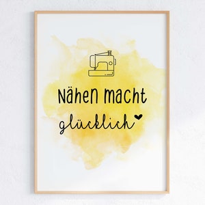 Könnte beinhalten: Gerahmter Druck mit hellem Holzrahmen. Das Kunstwerk zeigt eine schwarze Strichzeichnung einer Nähmaschine über den Worten "Nähen macht glücklich" in schwarzer Schrift, vor einem gelben Aquarellhintergrund.