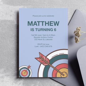 May include: A pale blue birthday invitation with the text "MATTHEW IS TURNING 6". The invitation includes party details: date, time, and location. The design features a target and arrow graphic, perfect for an archery-themed party.