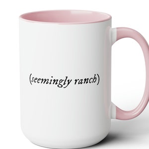 May include: White ceramic mug with a pink rim and handle. The mug has the text "(seemingly ranch)" printed on the front in black.