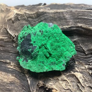 May include: A green and black malachite rock specimen. The rock has a rough, textured surface and is irregularly shaped.