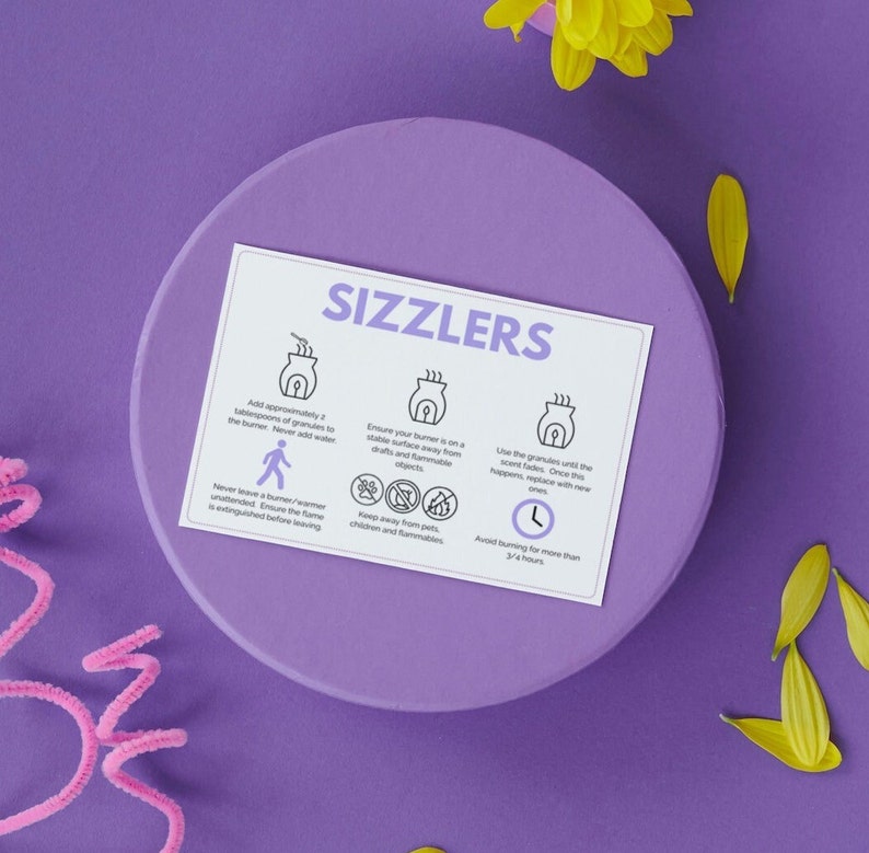 May include: A white card with the word "Sizzlers" in black text at the top. The card has instructions for using a wax warmer, including adding granules, keeping it away from flammable objects, and avoiding burning for more than 3 1/2 hours.