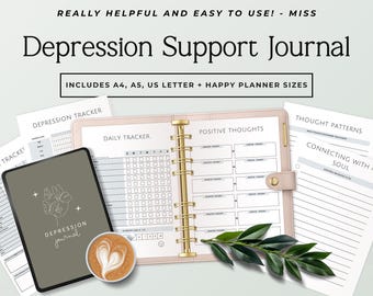Può includere: Un diario di supporto per la depressione con un raccoglitore rosa chiaro, anelli dorati e diverse pagine stampate tra cui un tracker giornaliero e schemi di pensiero. Sono visibili una cover per tablet verde scuro con disegno a linee e un caffè.