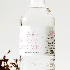 May include: A clear plastic water bottle with a white label. The label has a pink and white design with a snowy pine tree and the text "Sandra's Baby Shower" and "December 14th, 20xx".