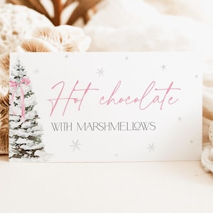 May include: A white card with a pink watercolor illustration of a Christmas tree with a pink ribbon. The text on the card reads "Hot chocolate with marshmallows".