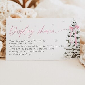 May include: A white card with pink text that says "Display shower" and a watercolor illustration of a snowy Christmas tree with a pink bow. The text on the card reads: "Your thoughtful gift will be shown on display. So there is no need to wrap it in any way. A ribbon or twine will do just fine leaving us with more time to visit and dine."