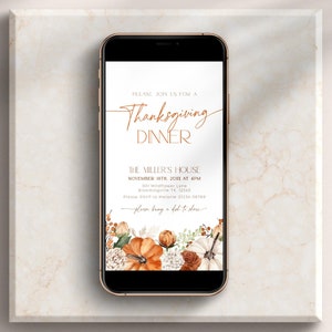 Könnte beinhalten: Ein Smartphone zeigt eine Einladung zum Thanksgiving-Dinner. Die Einladung hat eine elegante Kalligraphie und florale Akzente mit Kürbissen und Herbstlaub. Der Text lautet "Thanksgiving Dinner" und enthält Eventdetails.