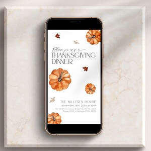 Puede incluir: Un smartphone muestra una invitación a una cena de Acción de Gracias. La invitación presenta calabazas en acuarela y hojas de otoño. El texto dice "Please join us for a Thanksgiving Dinner" y "The Miller's House". El teléfono está sobre una superficie de mármol.
