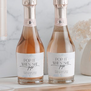 Op de afbeelding: Twee mini-flessen mousserende wijn met witte etiketten waarop staat "Pop it when she pops" en "Enjoy a toast when baby Miller arrives".