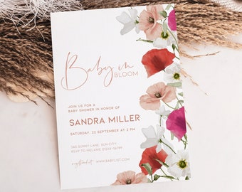 Op de afbeelding: Een baby shower uitnodiging met een bloemenontwerp. De uitnodiging is wit met roze en rode bloemen en de tekst "Baby in Bloom" in roze handschrift. De tekst bevat ook de naam "Sandra Miller", de datum "Zaterdag 22 september om 14:00 uur" en het adres "340 Sunny Lane, Sun City".