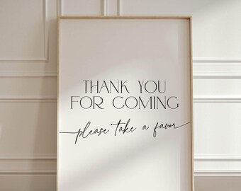 Puede incluir: Un letrero enmarcado con el texto "THANK YOU FOR COMING please take a favor" en escritura negra. El letrero tiene un fondo beige claro y un marco delgado, marrón claro. Está apoyado contra una pared blanca y un suelo de madera.