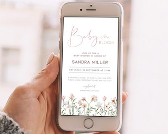 May include: A smartphone displays a baby shower invitation. The invitation features the text "Baby in Bloom" in elegant script, along with details for Sandra Miller's baby shower. Floral illustrations border the bottom of the screen.