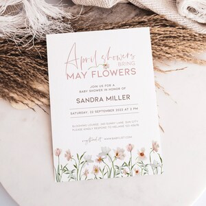 May include: A white baby shower invitation with pink calligraphy that reads "April showers bring May flowers". The invitation includes details for a baby shower in honor of Sandra Miller on September 22nd at 2 PM. The invitation features a floral design with pink and white flowers.