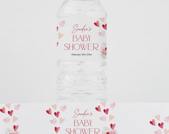 Könnte beinhalten: Eine transparente Plastikwasserflasche mit weißem Deckel und einem Etikett mit der Aufschrift "Sandra's BABY SHOWER" in roter Schrift, mit roten und rosa Herzillustrationen. Ein passendes Etikett befindet sich unter der Flasche.