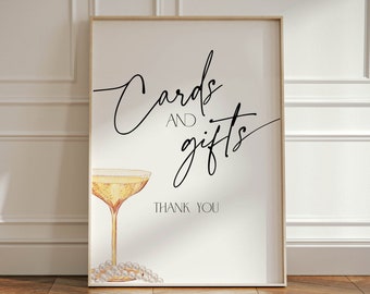 Könnte beinhalten: Ein weißes Schild mit schwarzer Kalligraphie, auf dem "Karten und Geschenke" steht, darunter eine Champagnerflöte und Perlen. Das Schild trägt den Schriftzug "Vielen Dank" unten.