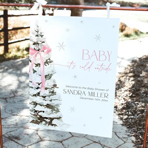 May include: A white sign with a watercolor illustration of a snowy pine tree with a pink ribbon. The sign reads "BABY it's cold outside" and "Welcome to the Baby Shower of SANDRA MILLER December 14th, 20xx".
