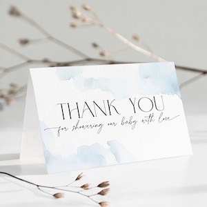 Może przedstawiać: Biała kartka z podziękowaniem z niebieskim akwarelowym tłem. Tekst na kartce brzmi: "Dziękujemy za obdarowanie naszego dziecka miłością."
