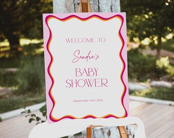 May include: Welcome to Sandra's Baby Shower sign with pink, orange and white wavy borders. The sign is on an easel and says "Welcome to Sandra's Baby Shower" with the date "September 14th, 20xx".
