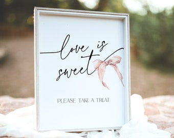 May include: White sign with the text "Love is sweet" in black cursive font. A pink ribbon with a bow is on the sign. The text "Please take a treat" is below the ribbon.