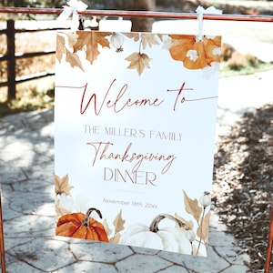May include: A Thanksgiving dinner welcome sign with the text "Welcome to The Miller's Family Thanksgiving Dinner" in a script font. The sign features watercolor pumpkins, leaves, and the date November 18th, 20xx. The sign is hanging on a copper-colored metal stand.