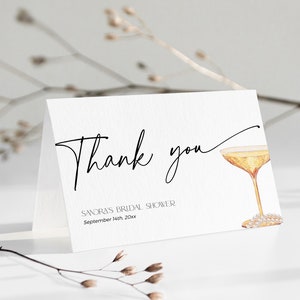 May include: Thank you card with a black and white calligraphy font. The card features a watercolour illustration of a champagne flute with a pearl necklace. The text on the card reads "Thank you" and "Sandra's Bridal Shower, September 14th 20xx".
