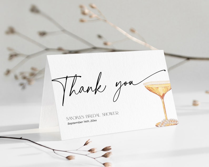 May include: Thank you card with a black and white calligraphy font. The card features a watercolour illustration of a champagne flute with a pearl necklace. The text on the card reads "Thank you" and "Sandra's Bridal Shower, September 14th 20xx".