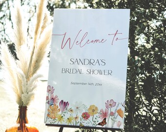 May include: A white sign with pink text that says "Welcome to Sandra's Bridal Shower" and the date "September 14th, 20xx". The sign is decorated with a watercolor border of flowers and butterflies.