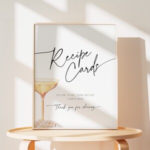 May include: A printable sign with a champagne glass and the text "Recipe Cards" in a cursive font. The sign says "Please leave your recipe cards here. Thank you for sharing."