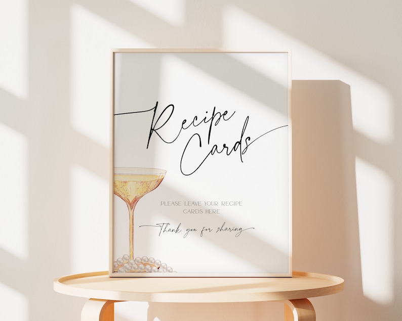 May include: A printable sign with a champagne glass and the text "Recipe Cards" in a cursive font. The sign says "Please leave your recipe cards here. Thank you for sharing."