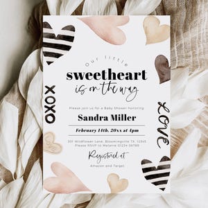 May include: A baby shower invitation with a white background and black and white hearts. The text reads "Our little sweetheart is on the way." The invitation also includes the date, time, and location of the shower. The text "Registered at Amazon and Target" is also included.