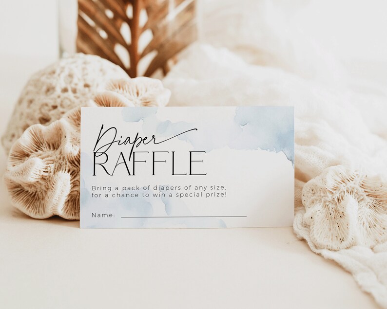 May include: A white rectangular card with the words "Diaper RAFFLE" in black script and sans-serif font. The card has a watercolor blue wash design. Text below reads "Bring a pack of diapers of any size... for a chance to win a special prize!"