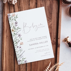 May include: A white baby shower invitation with a floral border and the text "Baby in Bloom". The invitation includes the name "Sandra Miller", the date "Saturday, 22 September at 2 PM", the address "340 Sunny Lane, Sun City", and the RSVP information "RSVP to Melanie 01234-56789". The invitation also includes the website "www.babylist.com".