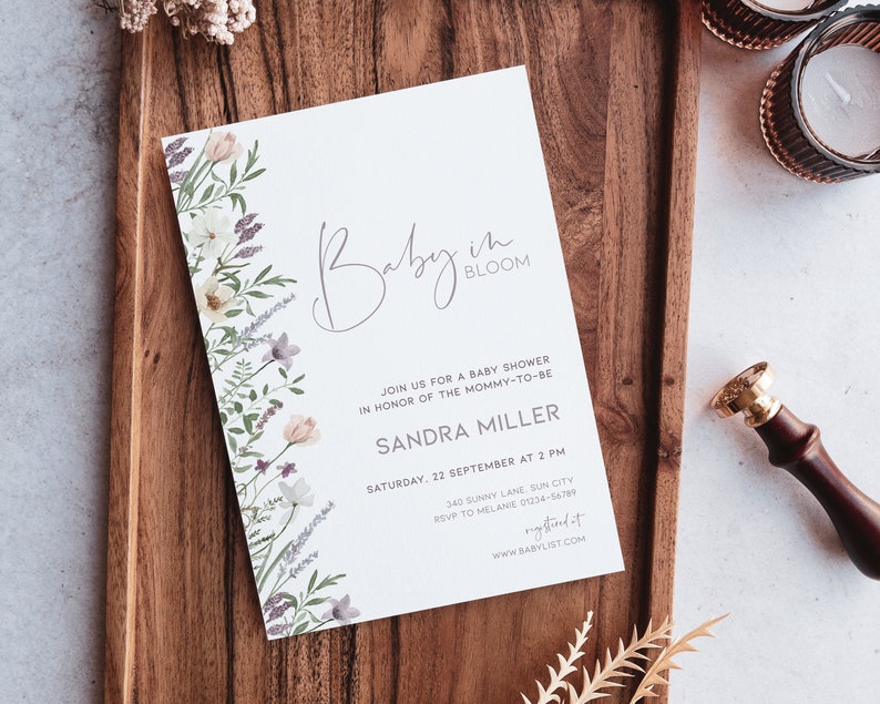 May include: A white baby shower invitation with a floral border and the text "Baby in Bloom". The invitation includes the name "Sandra Miller", the date "Saturday, 22 September at 2 PM", the address "340 Sunny Lane, Sun City", and the RSVP information "RSVP to Melanie 01234-56789". The invitation also includes the website "www.babylist.com".