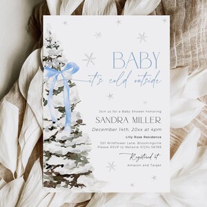 May include: A blue and white baby shower invitation with a watercolor illustration of a snow-covered pine tree with a blue ribbon. The text reads "Baby it's cold outside" and includes details for the event, including the date, time, location, and RSVP information. The invitation also includes the text "Registered at Amazon and Target".