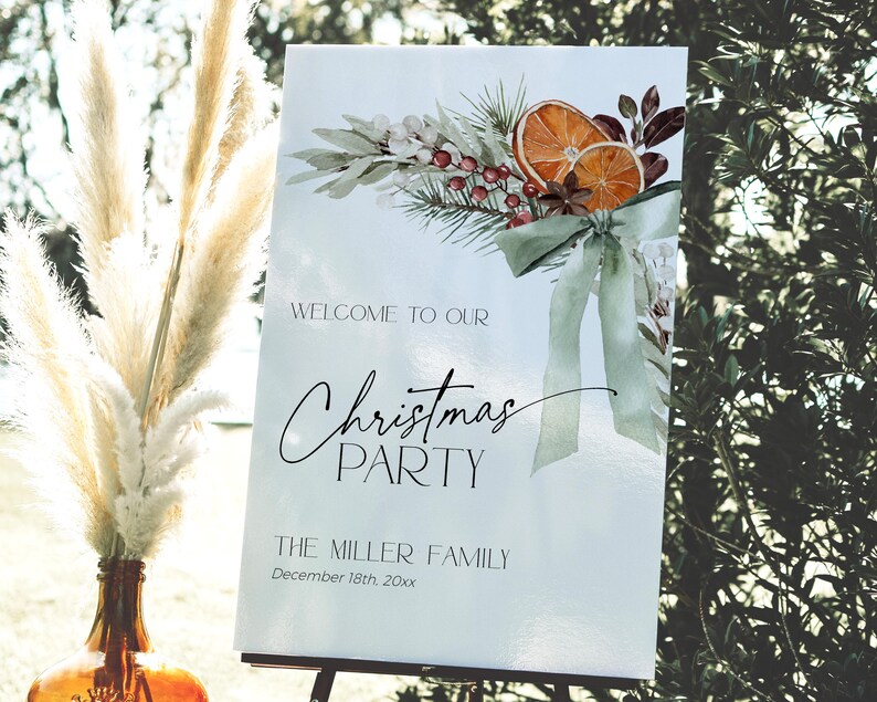 May include: A white sign with a watercolor illustration of a green wreath with orange slices, berries, and a green bow. The text on the sign reads "Welcome to our Christmas Party The Miller Family December 18th, 20xx".