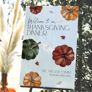 May include: Thanksgiving dinner welcome sign with watercolor pumpkins in orange, green, and red. The sign includes the text "Welcome to our Thanksgiving Dinner" and family name and date.