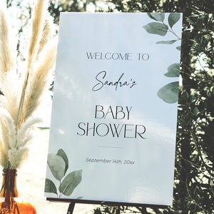 May include: White sign with green watercolor leaves and the text "Welcome to Sandra's Baby Shower September 14th, 20xx".